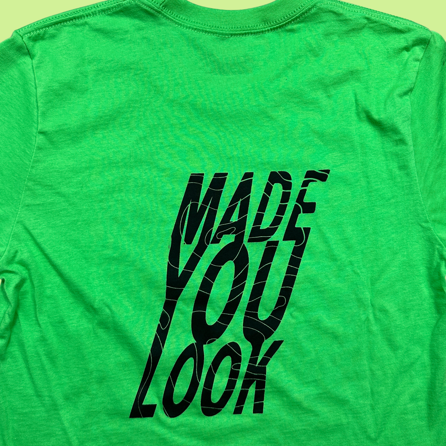 Closeup - Back of the bright green cropped tee with "made you look" in big block letters with a line that runs through all the words. The design is black.
