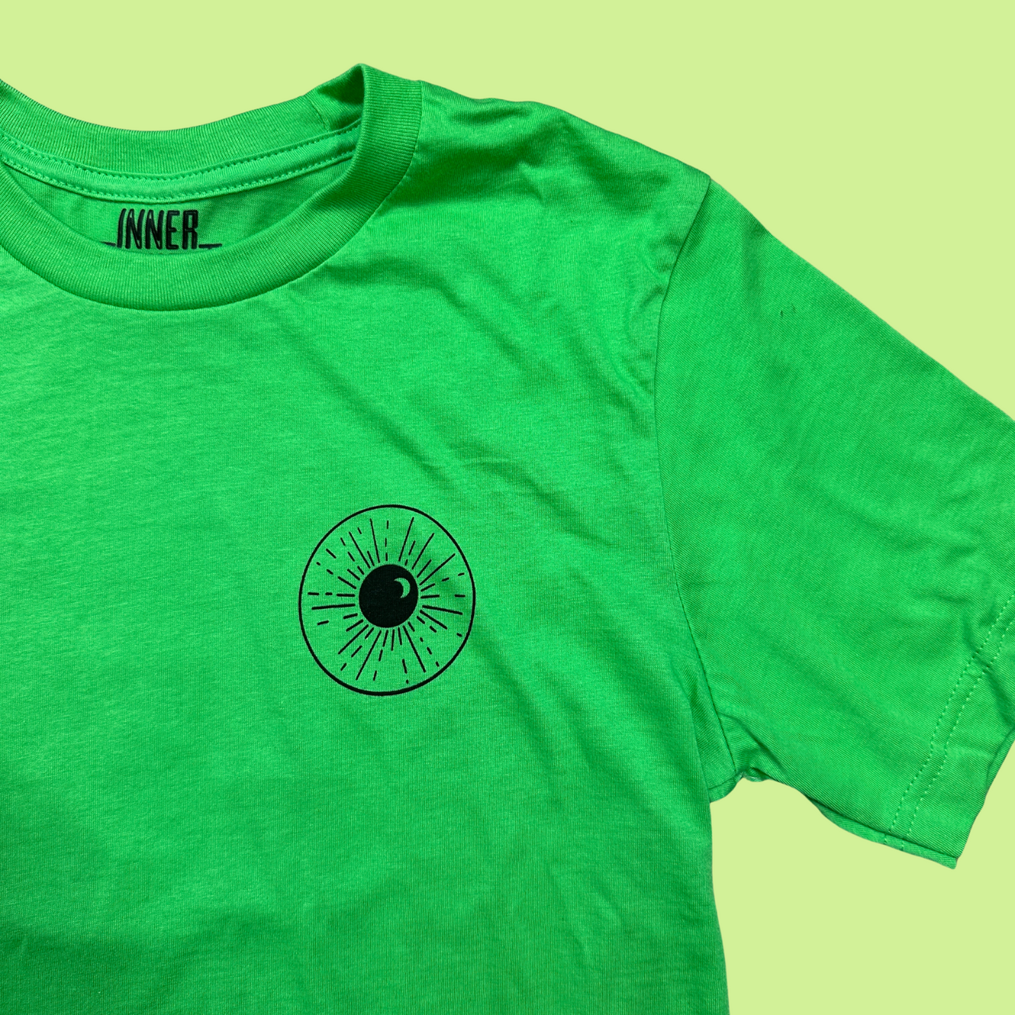 Closeup - Bright green cropped tee with a minimalistic eye and night sky design on the front area where a pocket would be. The design is black.