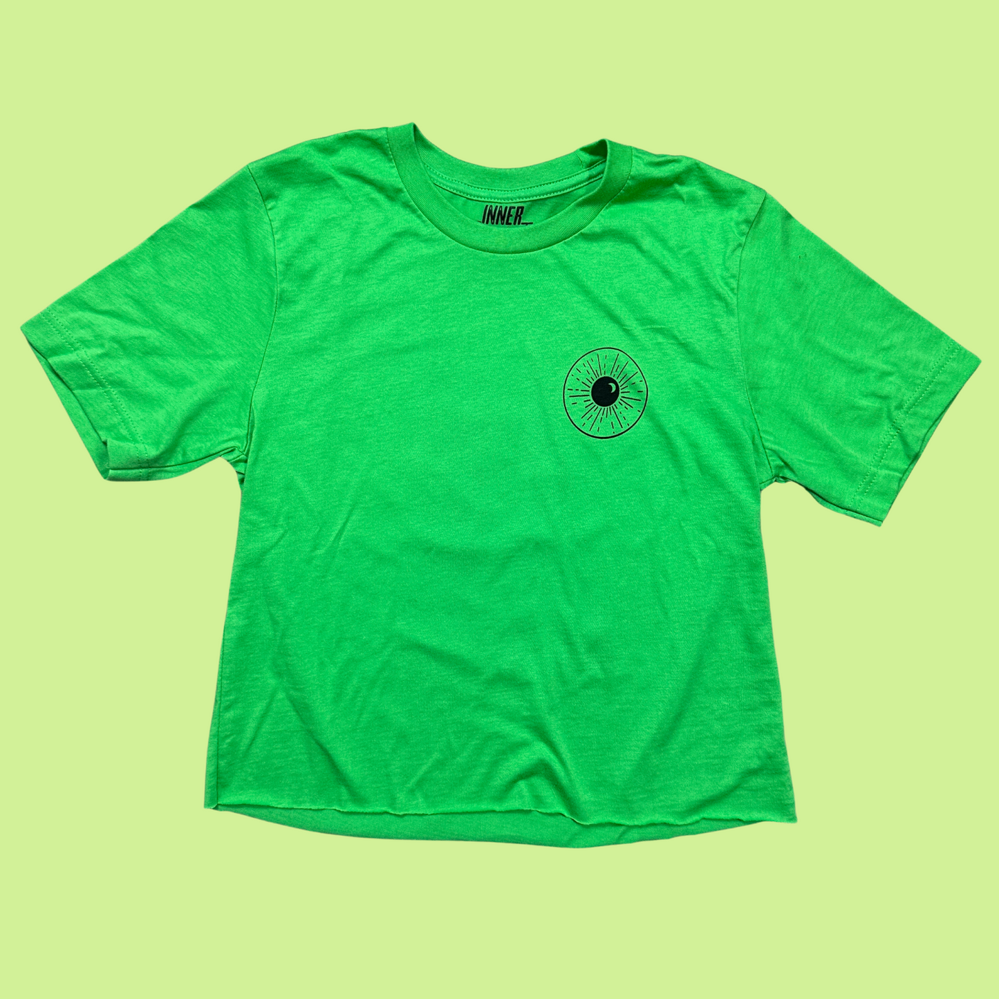 Bright green cropped tee with a minimalistic eye and night sky design on the front area where a pocket would be. The design is black.